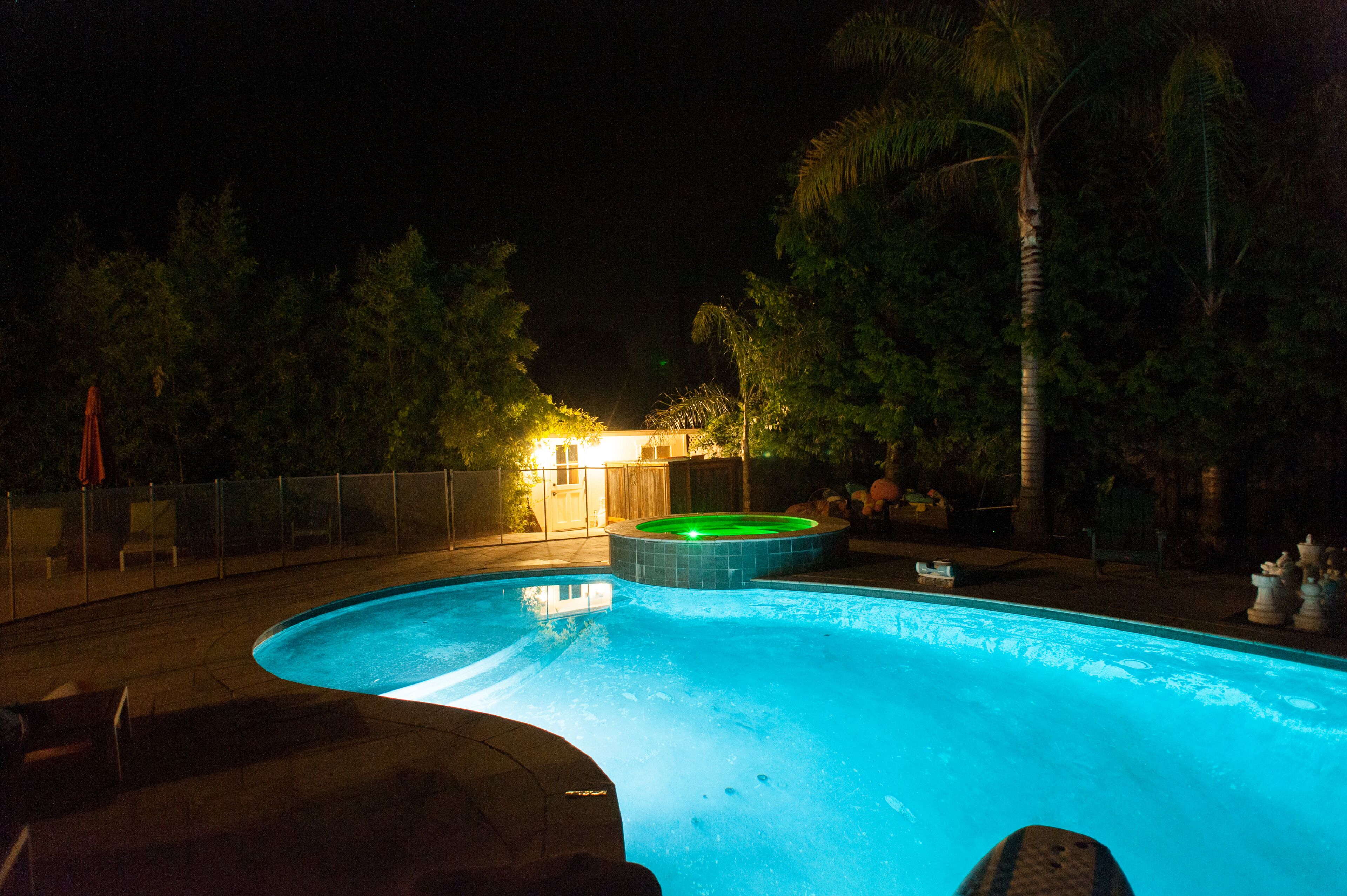 Ein Swimmingpool mit Whirlpool, umgeben von einem Zaun und Palmen.