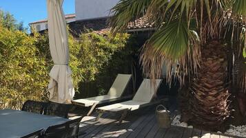 Relax on the deck surrounded by lush greenery and a palm tree, with a comfortable table and lounge chairs.