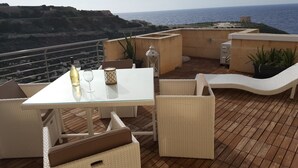 A terrace with a table set for two, wicker furniture, and potted plants.