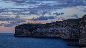 A coastal cliff with layered rock formations and a calm sea.
