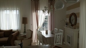 A living room with a sofa, a dining table with chairs, a chandelier, and a view through a window.