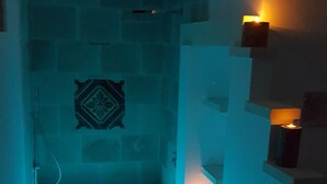 Une petite salle de bain à la lumière tamisée, dotée d’une douche, de murs carrelés et d’un élément décoratif mural.