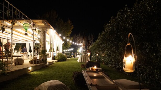 Un espace extérieur aménagé avec une terrasse, des guirlandes lumineuses, une plateforme en bois et une pelouse.