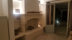 Une pièce chaleureuse avec une cheminée, une porte donnant sur l’extérieur et une petite étagère où sont posés quelques objets.