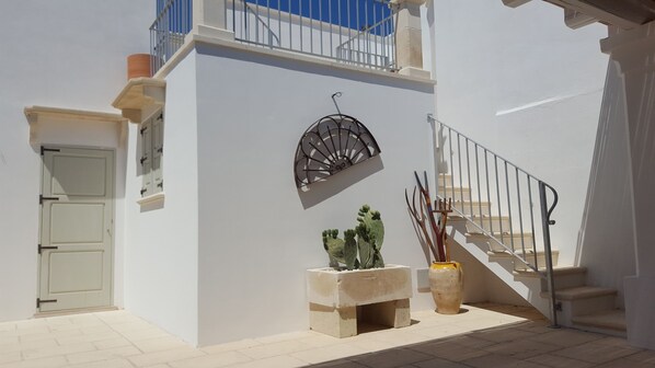 A white building with a balcony, a door, a staircase, and a decorative metal piece.