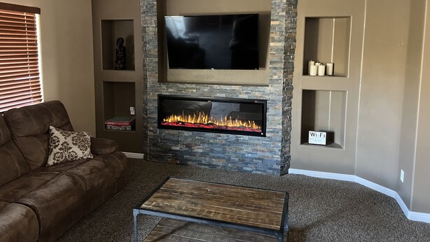 Una sala de estar con chimenea de piedra, un televisor de pantalla plana montado encima y un sofá de cuero marrón, junto con una mesa de centro.