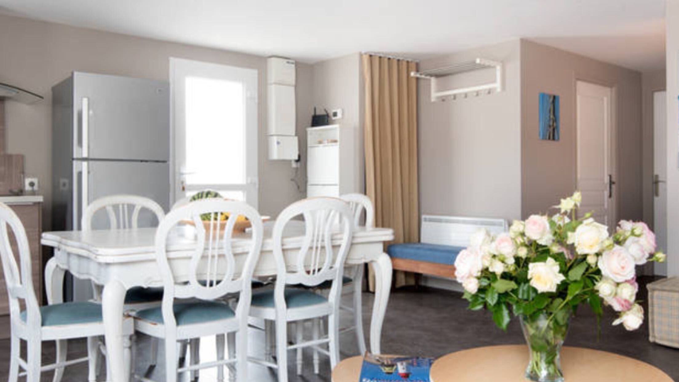 A modern kitchen with white appliances, a dining table with chairs, a small sofa, and a vase of flowers.