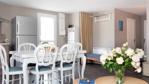 Una cucina moderna con elettrodomestici bianchi, un tavolo da pranzo con sedie, un piccolo divano e un vaso di fiori.