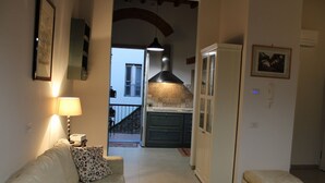 Una sala de estar con un sofá, una mesa de centro de vidrio y una cocina al fondo.