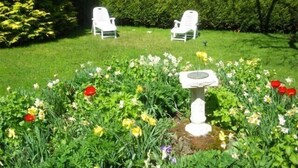 A garden with two white chairs, a birdbath, and various flowers.