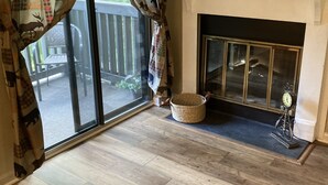 A room with a fireplace, a large window with curtains, a wicker basket, and a rug.