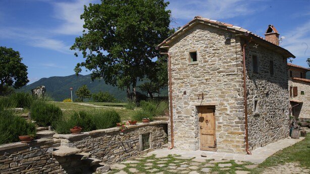 A stone building with a wooden door, surrounded by a stone wall and potted plants. - I Poggi di Belvedere (Pieve Santo Stefano AR)