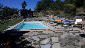 A rectangular pool with a stone deck surrounding it, equipped with lounge chairs and a small wooden structure in the background. - I Poggi di Belvedere (Pieve Santo Stefano AR)