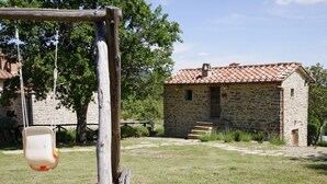 A stone building with a tiled roof, a swing set, and a grassy yard. - I Poggi di Belvedere (Pieve Santo Stefano AR)