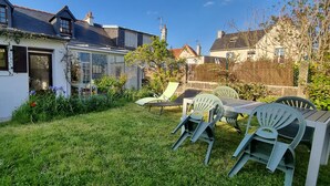 Une maison blanche avec une véranda en verre, une pelouse et du mobilier d’extérieur.