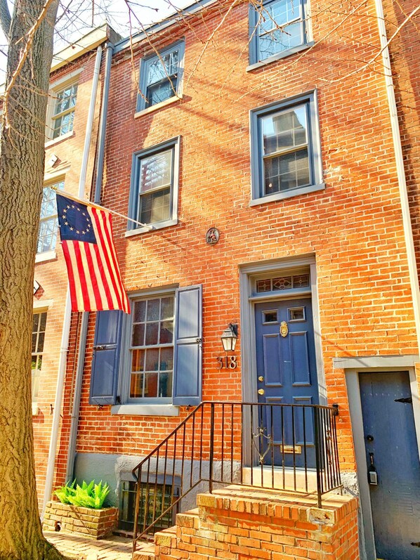 A brick building with a blue door, a number 318 sign, and an American flag.