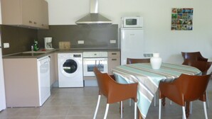 A compact kitchen with a washing machine, oven, microwave, and a dining area with chairs and a table. - Villa 500 m from Ste Marguerite beach (Pornichet)