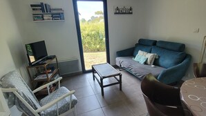 A living room with a sofa, a coffee table, a TV, and a bookshelf. There is a door leading outside. - Villa 500 m from Ste Marguerite beach (Pornichet)