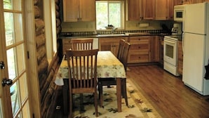 Une cuisine aménagée dans le style d’un chalet en rondins, avec des meubles de rangement en bois, une table à manger avec des chaises, un réfrigérateur et une cuisinière.