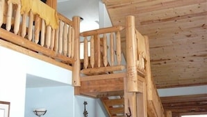 Un escalier en bois rustique avec une rampe en bois, un ventilateur de plafond et un lustre.