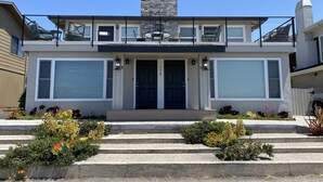 Une maison moderne à deux étages, dotée d’un balcon, de grandes fenêtres et d’une cheminée en pierre.