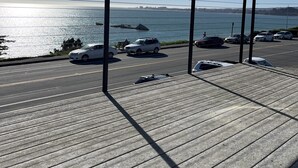 Une terrasse en bois offrant une vue sur la mer et les voitures garées.