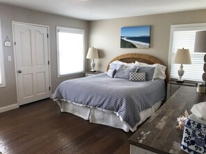 A bedroom with a large bed, two bedside lamps, a painting on the wall, and a door. - Beach House Overlooking Seacliff State Park and Rio Del Mar Beach, Aptos (Aptos)
