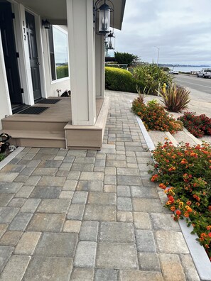 A building entrance with a stone-paved porch, a door with the number 172, and a row of flowering plants. - Beach House Overlooking Seacliff State Park and Rio Del Mar Beach, Aptos (Aptos)