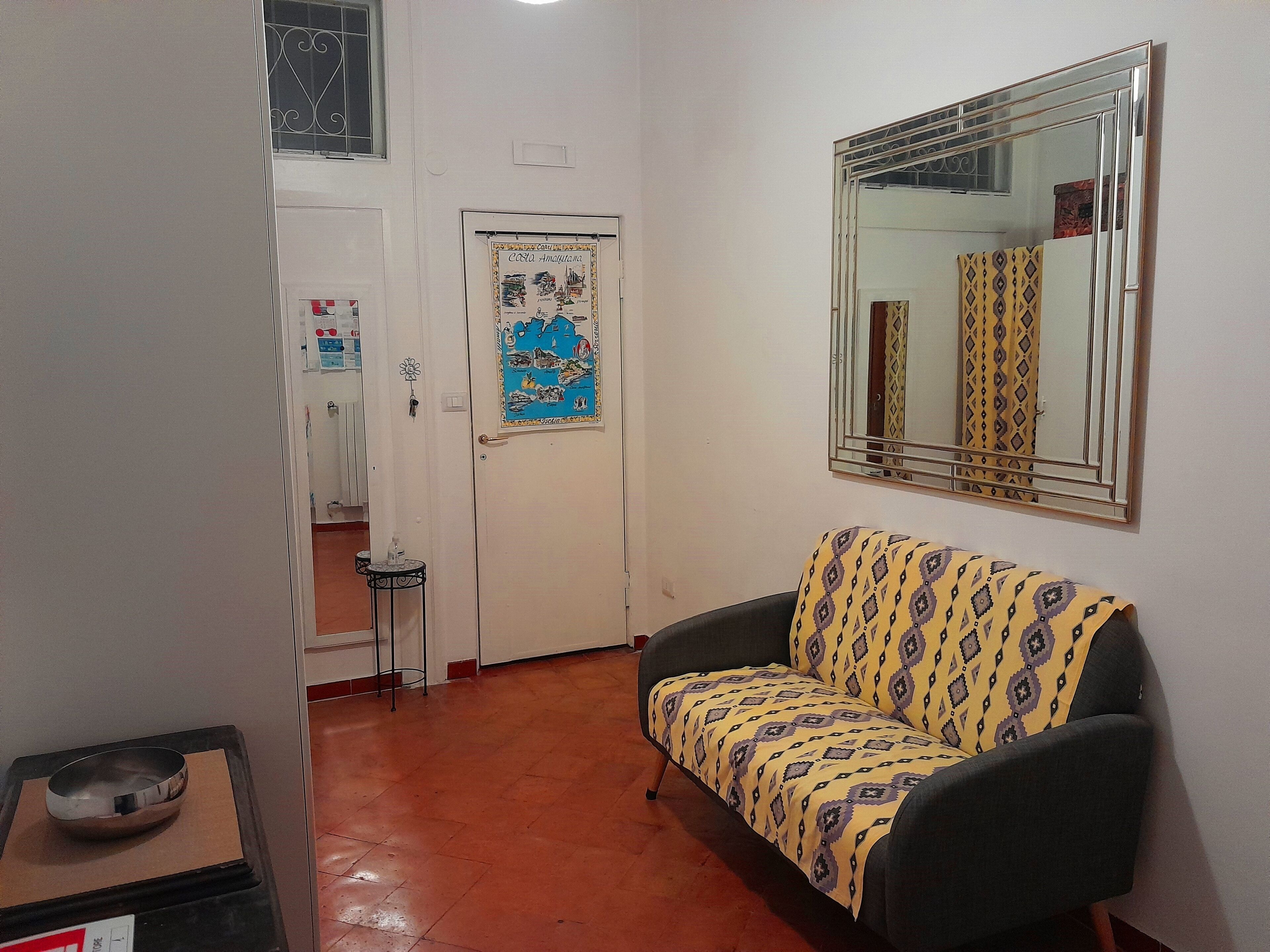 A hallway with a sofa, a door with a poster, a mirror, and a small table with a bowl.