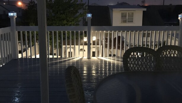 A deck with a white railing, a wicker chair, and a small table. - A Stone Throw Away from the Beach (Wildwood)