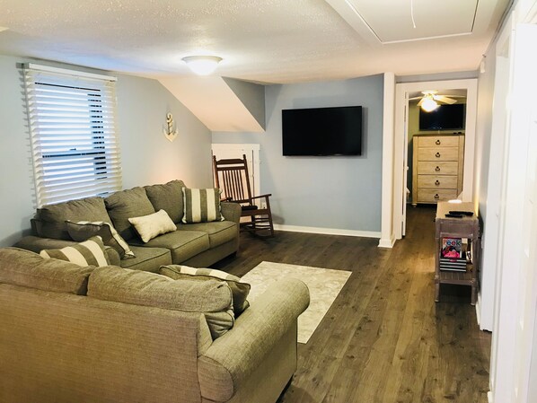 A living room with a sectional sofa, a flat-screen TV, and a wooden floor.