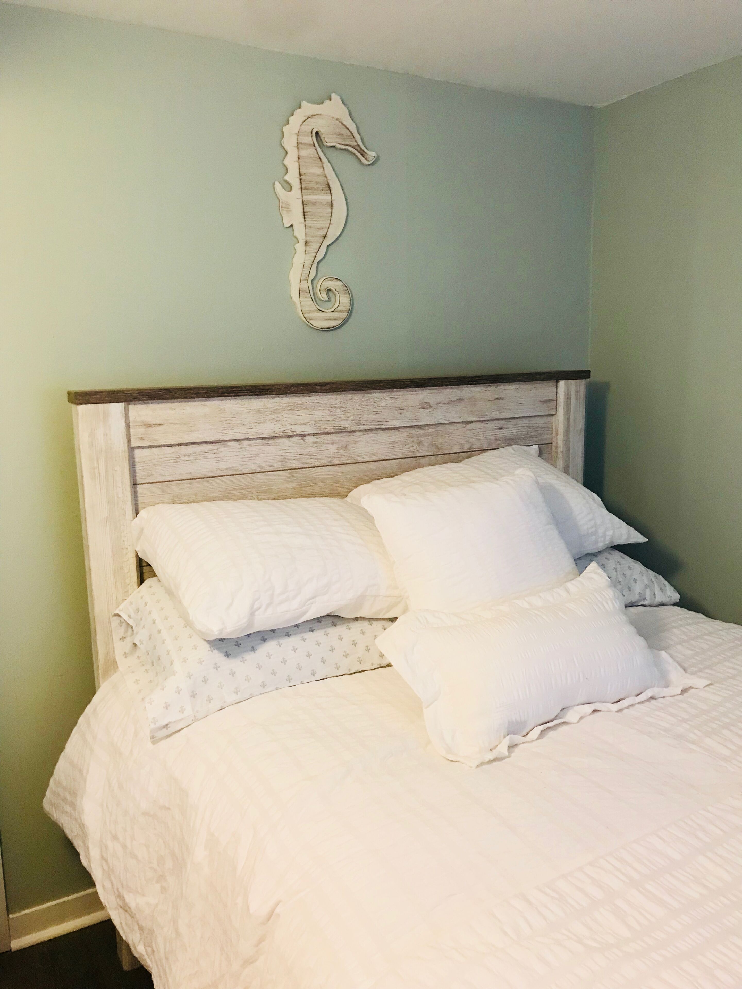 Un letto con biancheria bianca e una testiera in legno, una decorazione a forma di cavalluccio marino e pareti color verde chiaro.