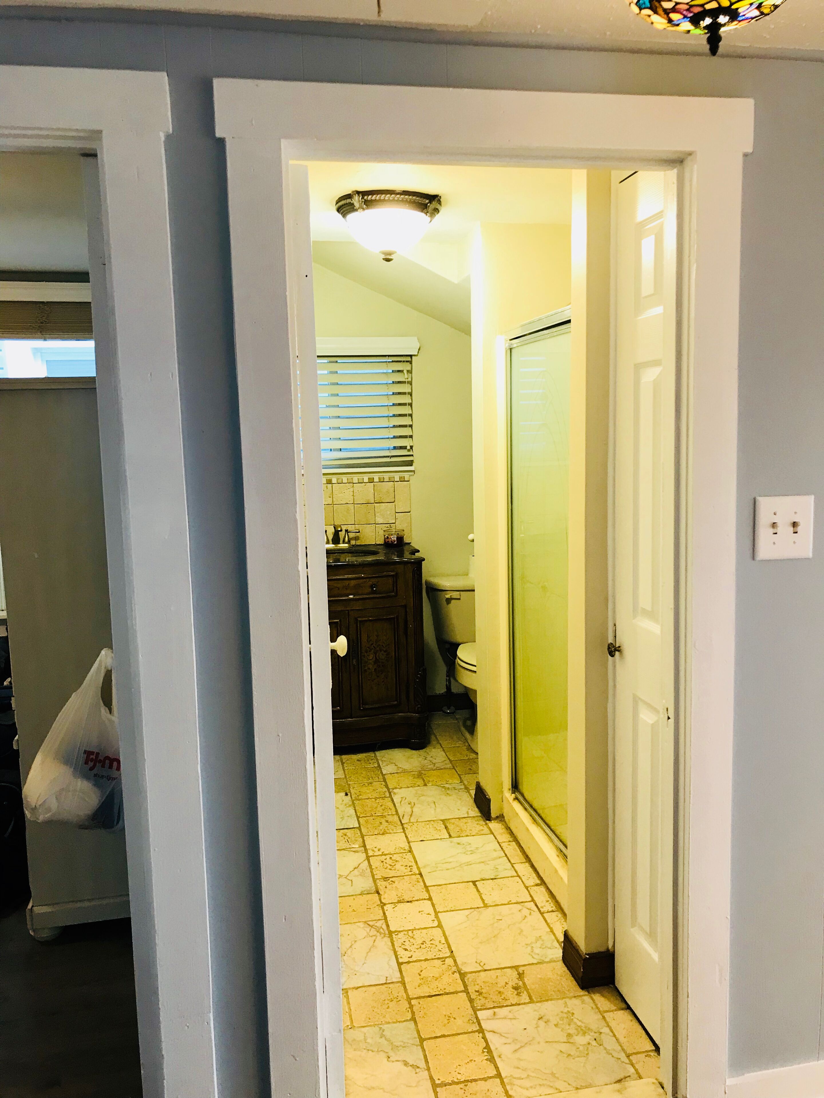 A narrow hallway with a tiled floor, a wooden cabinet, a toilet, and a glass shower door.