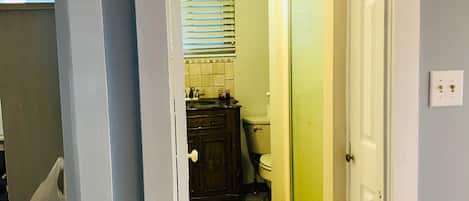 A narrow hallway with a tiled floor, a wooden cabinet, a toilet, and a glass shower door.