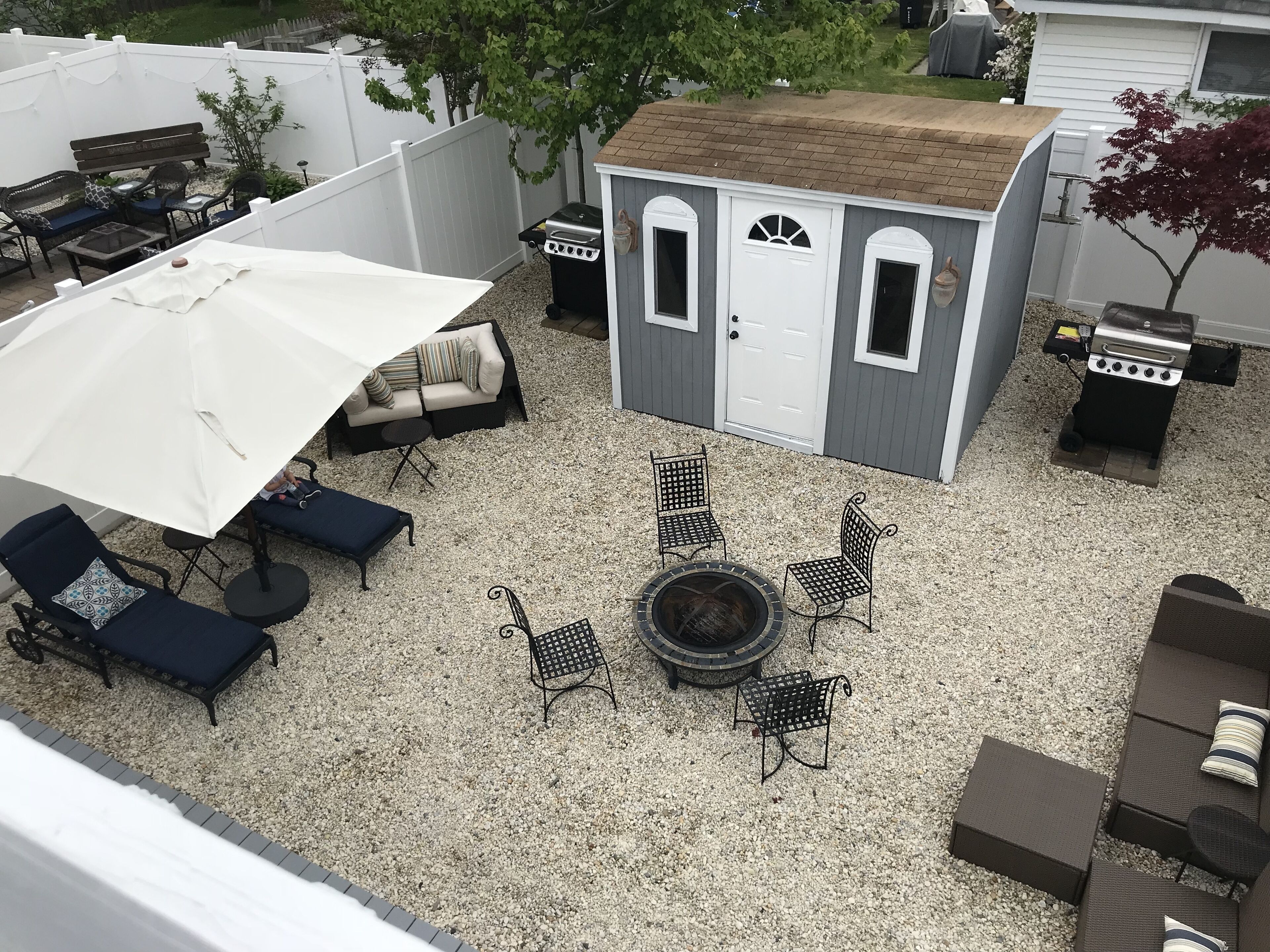 A backyard with a patio area featuring a white umbrella, a sofa, and multiple chairs.