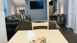 A compact living space with a dining table, a sofa, a TV mounted on the wall, and a kitchen area visible through an open door. - A Stone Throw Away from the Beach (Wildwood)