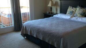 A bedroom with a large bed, a nightstand with a lamp, a painting on the wall, and a view through a window with curtains.