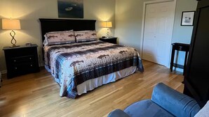 A bedroom with a bed, two bedside tables, a nightstand, a chair, a door, and a wall-mounted light fixture. - Lakeside Haven, Cottage#4, Pool, Hot Tub, Lake View (Taylorsville)