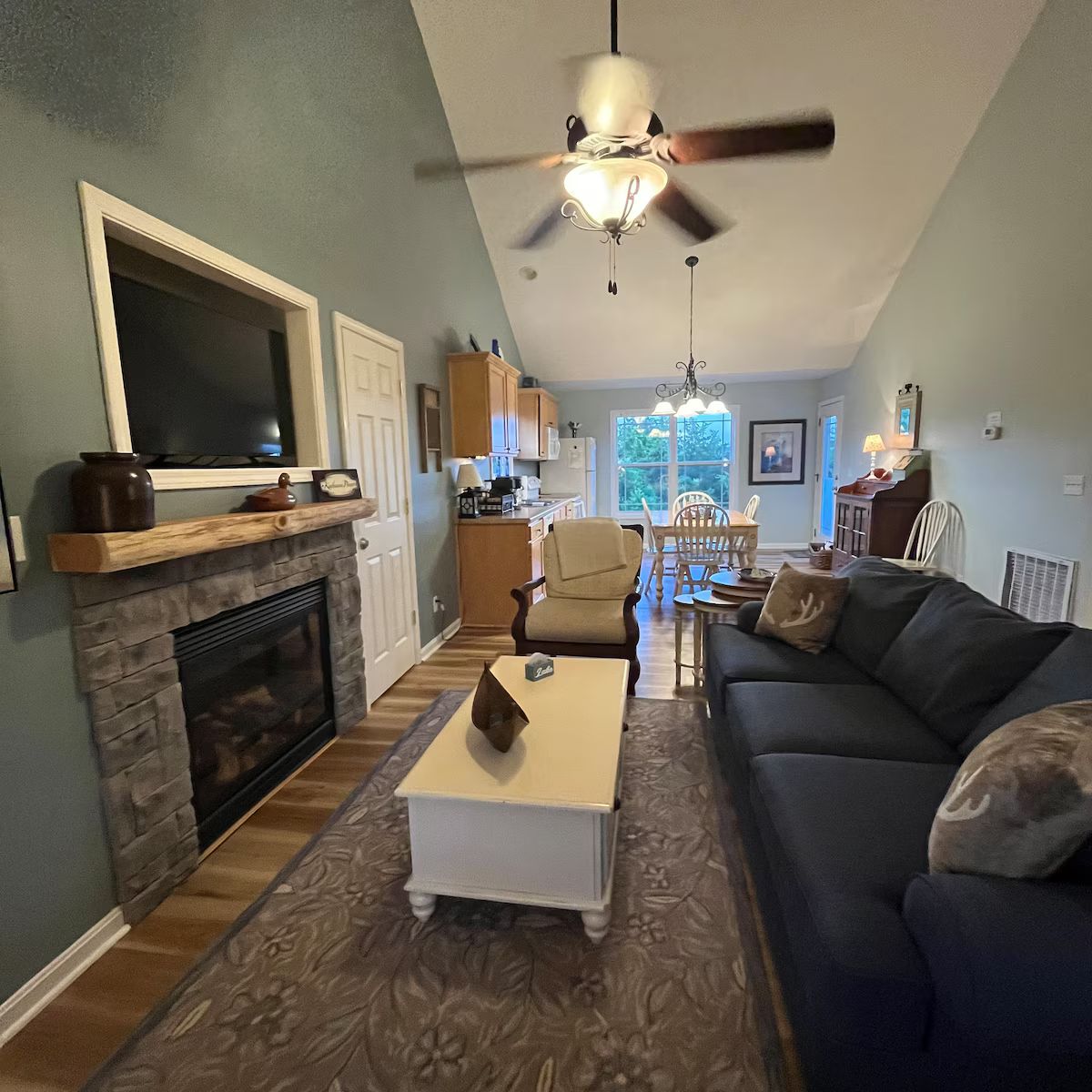 Una sala de estar con chimenea, televisor, ventilador de techo y comedor con mesa y sillas.