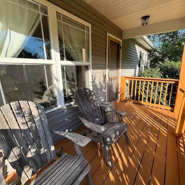 A wooden deck with Adirondack chairs, a wooden railing, and a window with curtains.