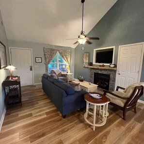 A living room with a sofa, a television, a fireplace, and a ceiling fan.