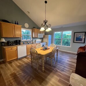 A kitchen with wooden cabinets, a dining table with chairs, a chandelier, and a view of greenery outside. - Lakeside Haven, Cottage#4, Pool, Hot Tub, Lake View (Taylorsville)