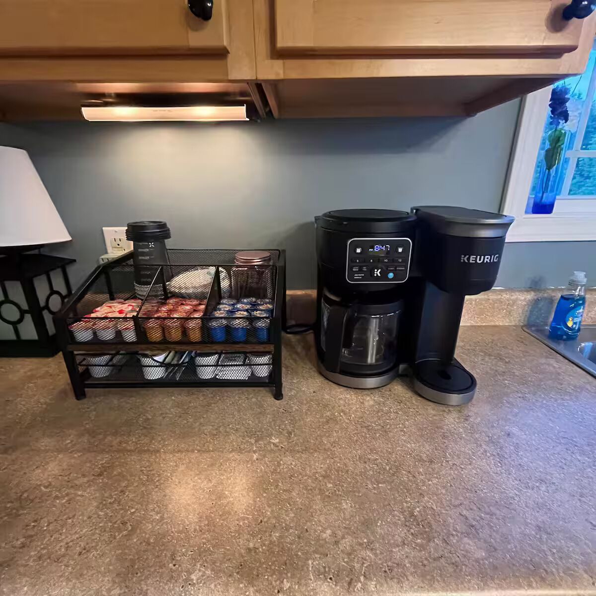 Una cocina con cafetera, un recipiente de malla con frascos y una encimera.