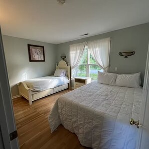 A bedroom with two beds, a window with curtains, a bedside table, and a wall-mounted light fixture.