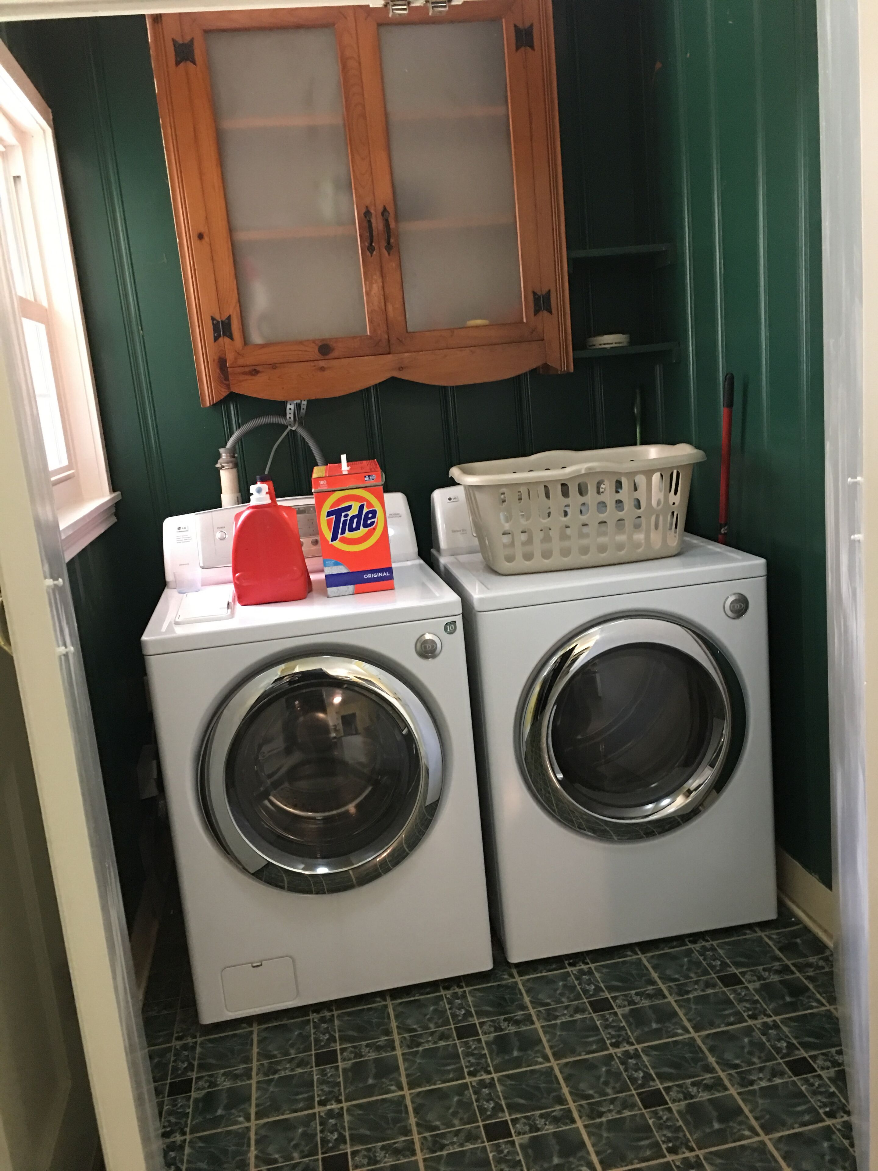 Een wasruimte met twee voorladers, een fles Tide wasmiddel, een wasmand en houten kastjes erboven.