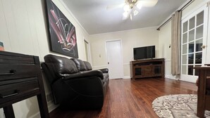 A living room with a black leather sofa, a flat-screen TV on a wooden stand, and a patterned rug. - A cozy single family home located right in the center of Augusta!  (Augusta)