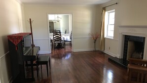 A spacious living room with hardwood flooring, a piano, a fireplace, and a dining area with a chandelier. - A cozy single family home located right in the center of Augusta!  (Augusta)