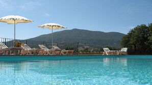 Une piscine aux eaux cristallines, bordée de chaises longues et d’ombrelles, entourée d’une clôture et avec une montagne en toile de fond.