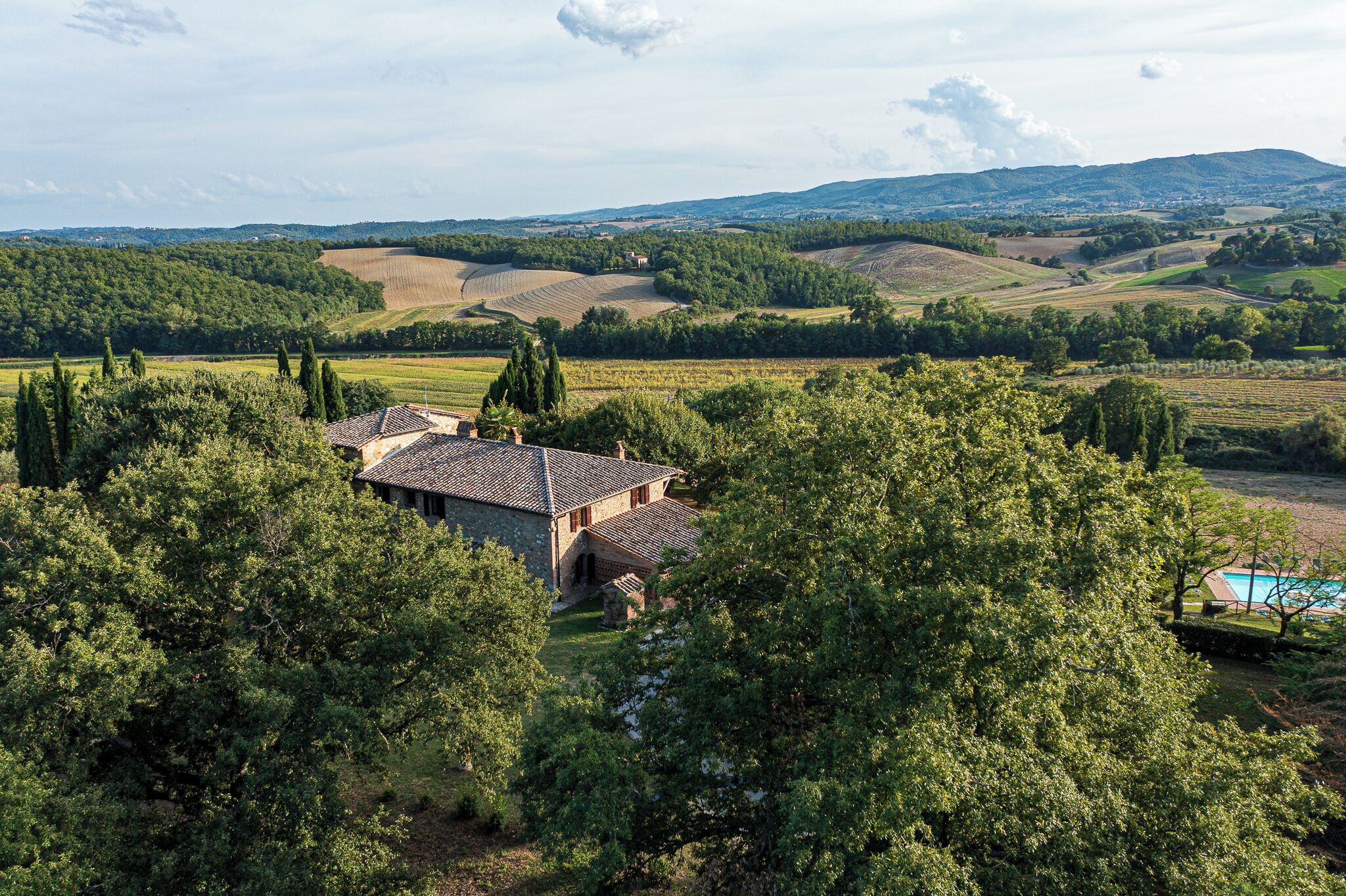 A stone house with a tiled roof surrounded by lush greenery and a swimming pool.