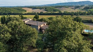Une maison en pierre, avec un toit de tuiles, entourée d’une végétation luxuriante et dotée d’une piscine.